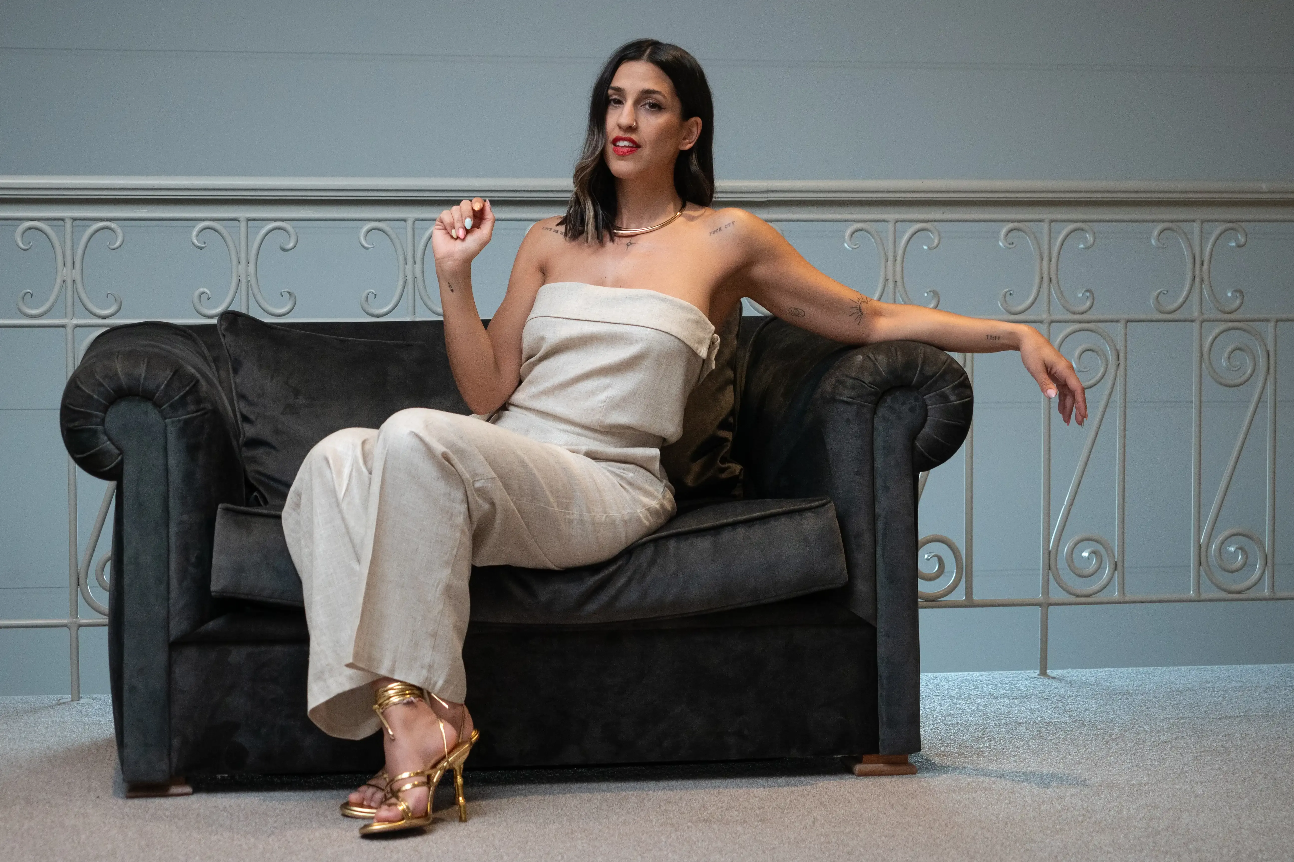 Uma mulher posa sentada num sofá vestida com um conjunto bege.